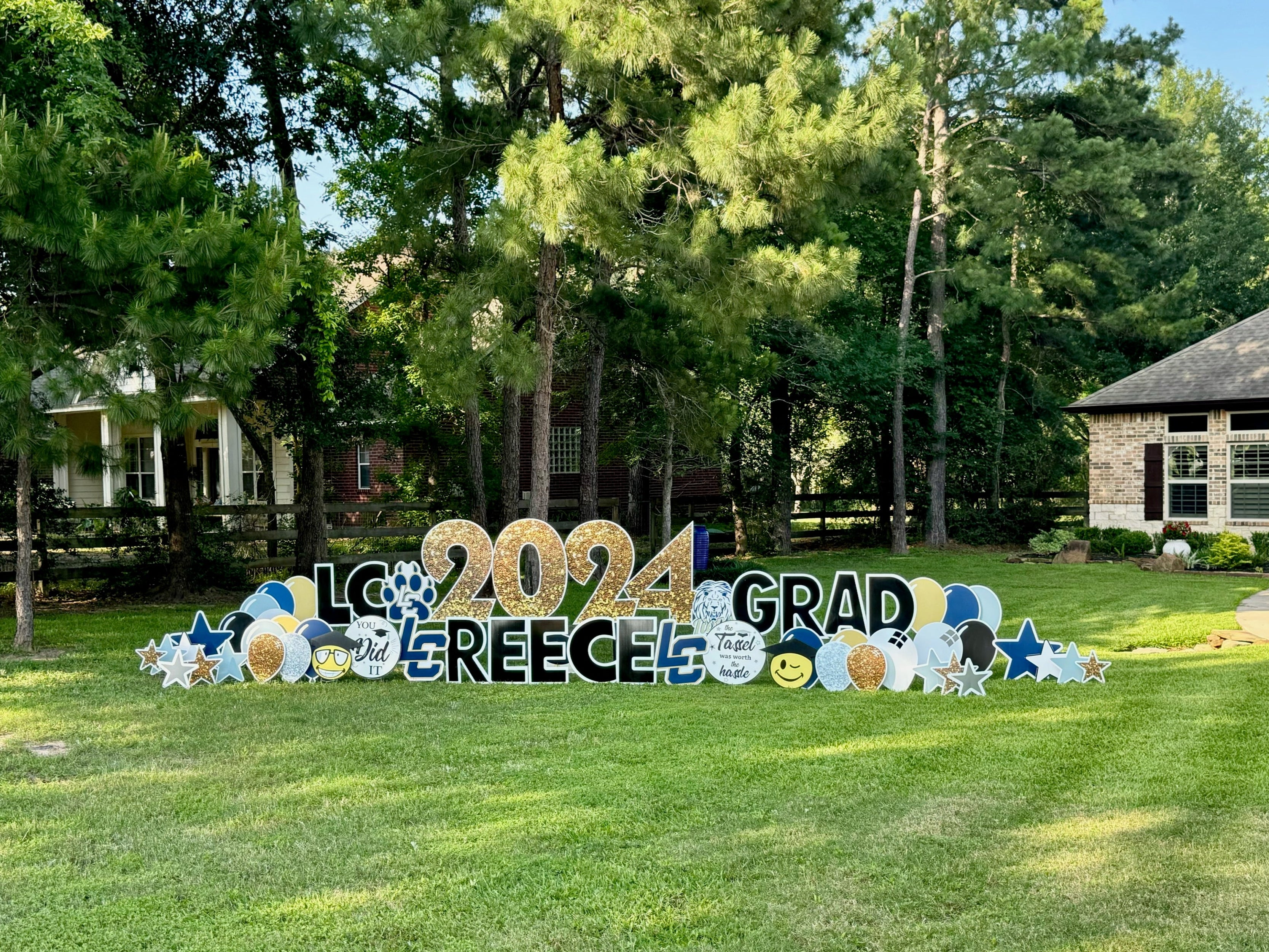 A celebratory yard card setup by Texas Party in the Yard, marking a high school graduation. The display includes a "Congrats Grad" message, the graduate's name, graduation caps, diplomas, and school colors, arranged in a front yard in Montgomery, TX.