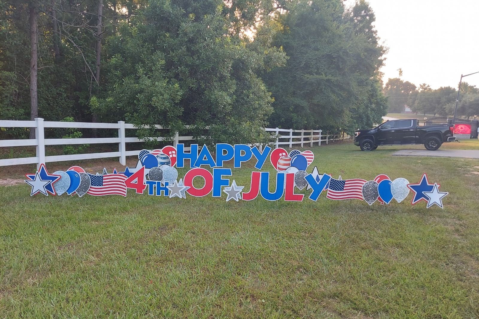 A festive yard card display by Texas Party in the Yard, celebrating a neighborhood July 4th event. The setup includes a "Happy 4th of July" message with American flags, fireworks, and patriotic graphics, creating a lively atmosphere in Montgomery, TX.