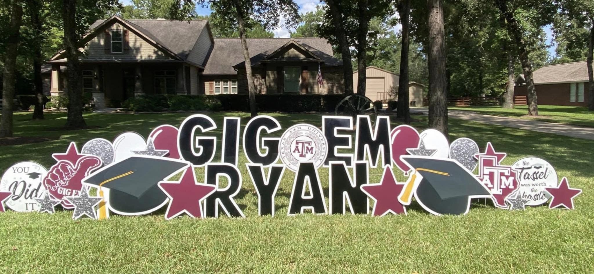 A proud yard card display by Texas Party in the Yard, celebrating a college graduation. The setup features a "Congratulations" message with the graduate's name, college colors, graduation caps, diplomas, and symbols representing their field of study, arranged in a yard in Montgomery, TX.