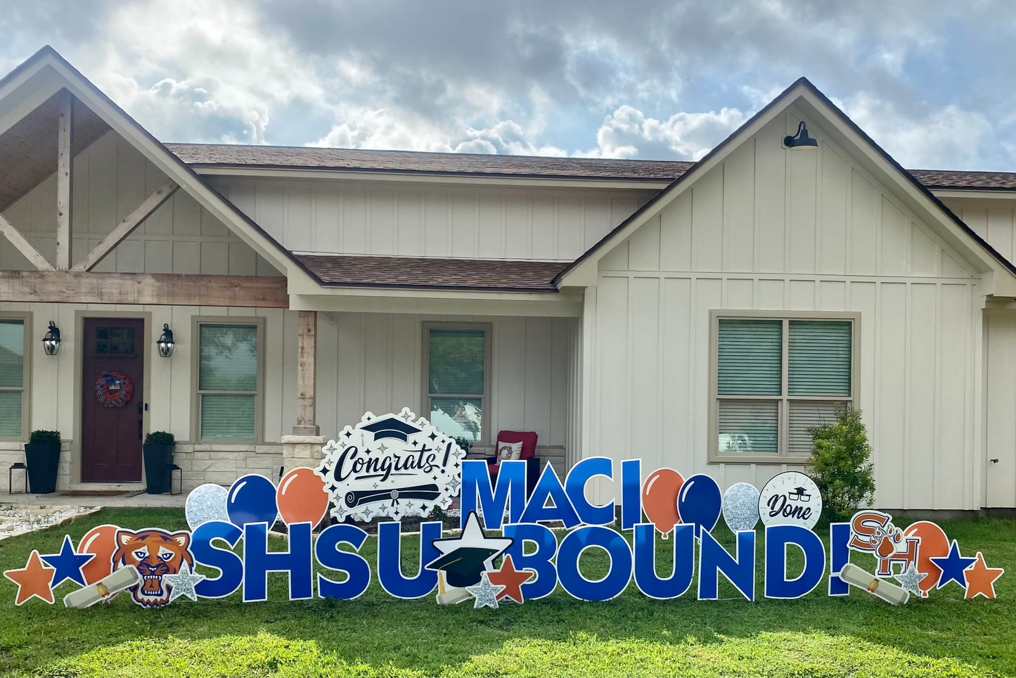 A proud yard card display by Texas Party in the Yard, celebrating a college graduation. The setup features a "Congratulations" message with the graduate's name, college colors, graduation caps, diplomas, and symbols representing their field of study, arranged in a yard in Montgomery, TX.