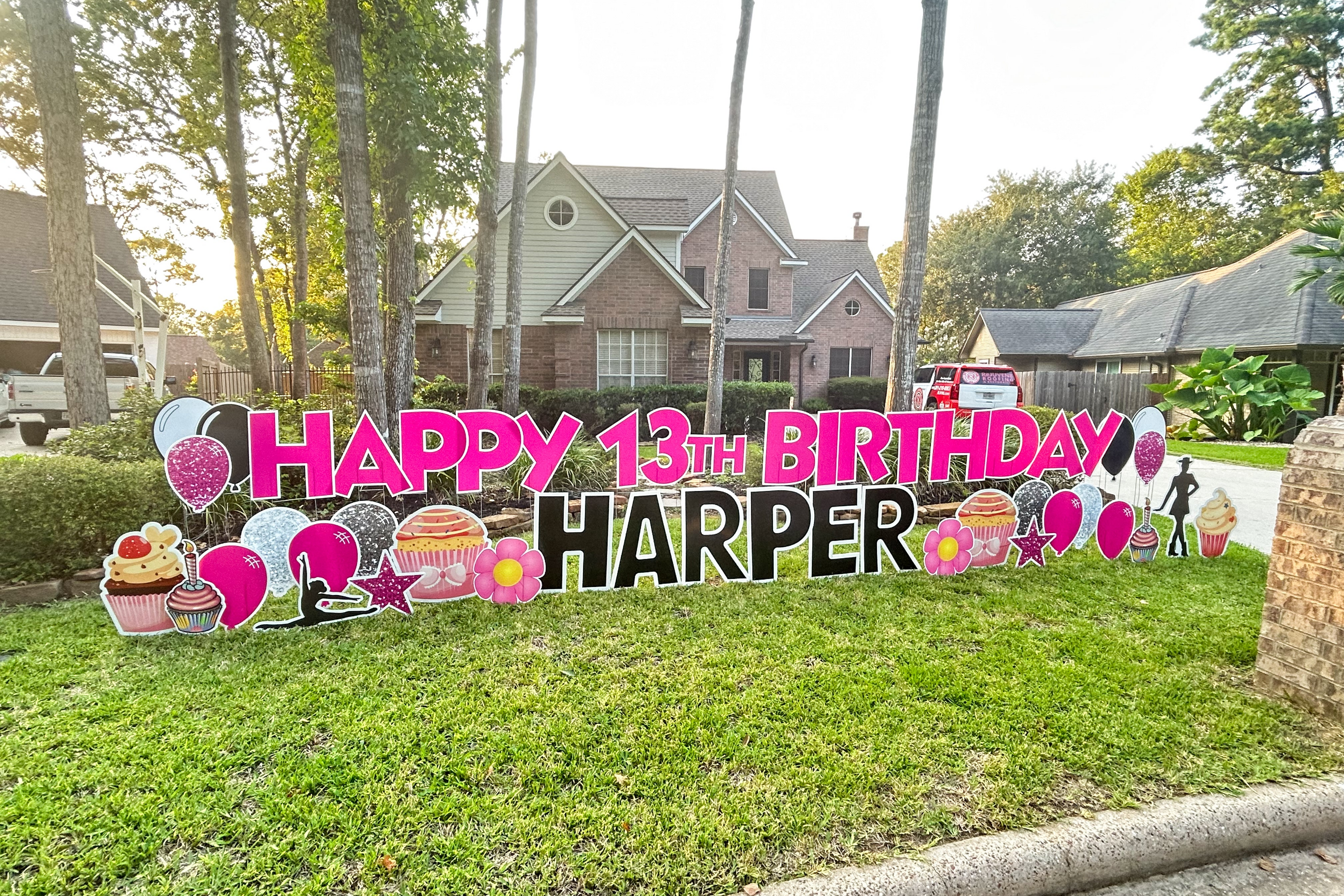 A vibrant yard card setup by Texas Party in the Yard, featuring a personalized "Happy Birthday" message with the birthday person's name, colorful balloons, bright stars, and festive graphic images. The display is arranged in a front yard, perfect for celebrating a special day in Montgomery, TX.