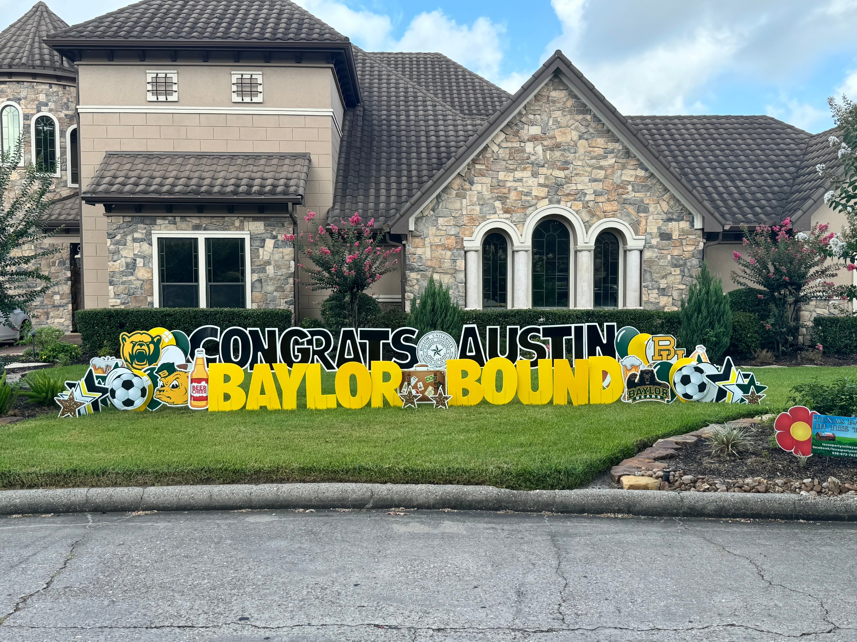 A proud yard card display by Texas Party in the Yard, celebrating a college graduation. The setup features a "Congratulations" message with the graduate's name, college colors, graduation caps, diplomas, and symbols representing their field of study, arranged in a yard in Montgomery, TX.